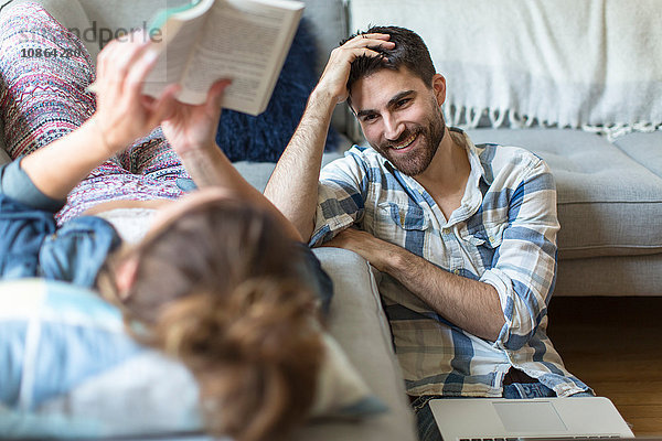 Junges Paar entspannt sich zu Hause  junge Frau auf Sofa liegend  junger Mann auf dem Boden sitzend  lachend