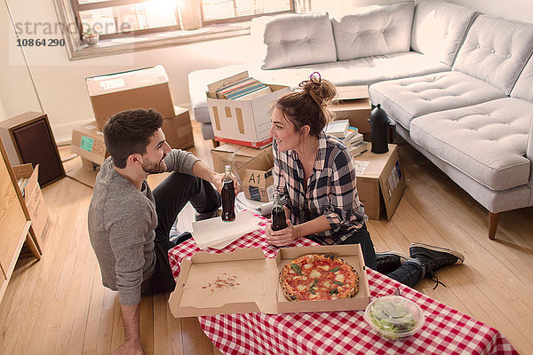 Umzug: Junges Paar isst Pizza im neuen Zuhause  umgeben von Kartons