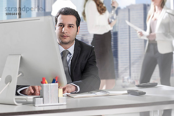 Geschäftsmann mit Computer im Büro  Kollegen chatten im Hintergrund