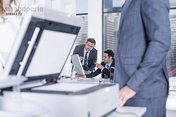 Geschäftsmann und Geschäftsfrauen unterhalten sich per Fotokopierer im Büro  Kollegen am Computer im Hintergrund