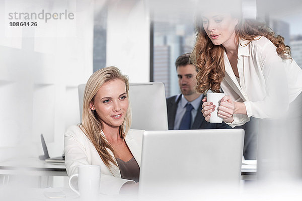 Geschäftsfrau benutzt Laptop im Büro  Kollegin benutzt Computer im Hintergrund