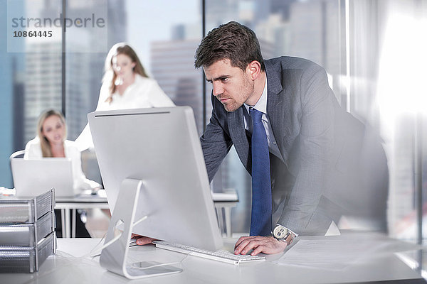 Geschäftsmann mit Computer im Büro  Kollegen arbeiten im Hintergrund