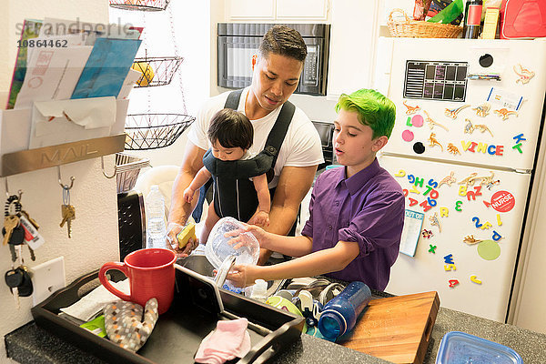 Sohn hilft Vater mit Baby im Gepäck beim Geschirrspülen