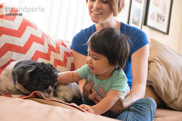 Mutter beobachtet Baby beim Spielen mit Hund auf dem Sofa