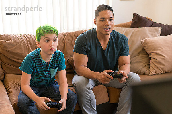 Vater und Sohn spielen Videospiel auf dem Sofa