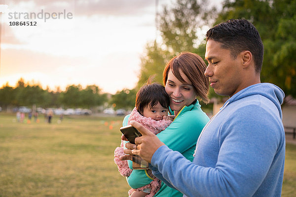 Paar mit Baby  mit Mobiltelefon im Park