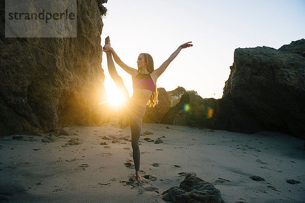 Junge Balletttänzerin balanciert auf einem Bein am sonnenbeschienenen Strand  Los Angeles  Kalifornien  USA