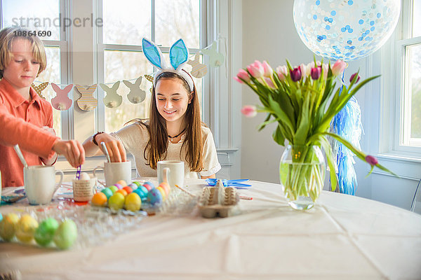 Teenager-Mädchen und Bruder färben hart gekochte Eier für Ostern bei Tisch