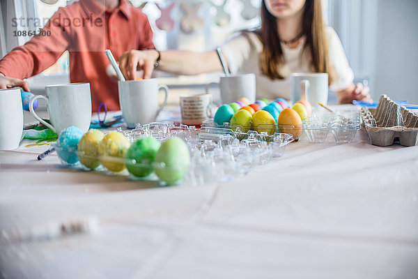 Schnappschuss eines Mädchens und eines Bruders im Teenageralter beim Tischfärben hart gekochter Eier für Ostern