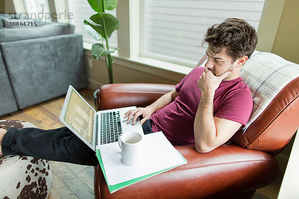 Mann auf Wohnzimmersessel mit den Füßen nach oben beim Arbeiten am Laptop