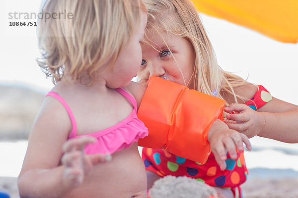 Mädchen bläst die aufblasbare Armbinde ihrer kleinen Schwester am Strand auf  Kapstadt  Südafrika