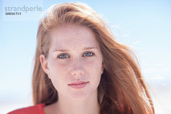 Bildnis einer schönen jungen Frau mit Sommersprossen und langen roten Haaren vor blauem Himmel