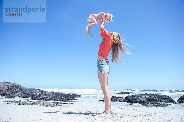 Junge Frau hält weibliches Kleinkind am Strand hoch  Kapstadt  Südafrika