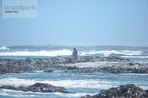 Distanzansicht eines jungen Paares  das sich am Strand umarmt  Kapstadt  Südafrika