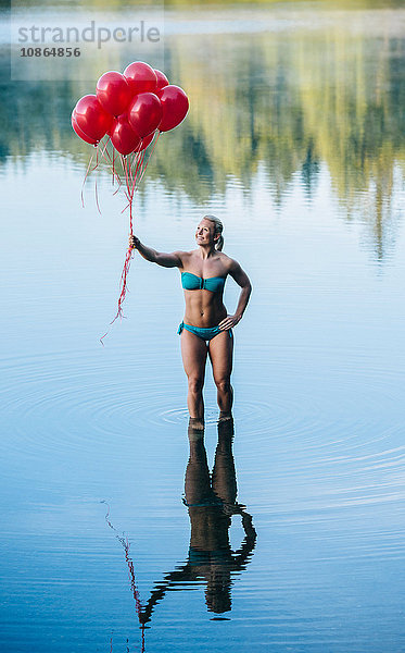 Frau knöcheltief im Wasser und hält einen Haufen roter Luftballons