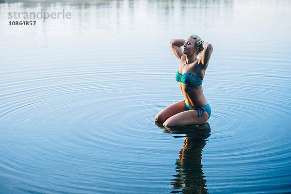 Im Wasser kniende Frau im Bikini