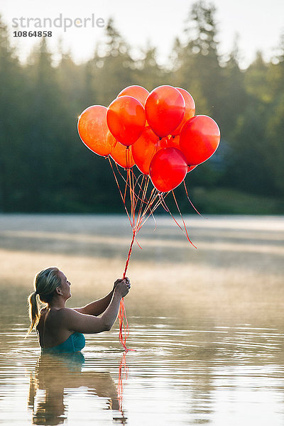 Frau im Wasser hält einen Haufen roter Luftballons