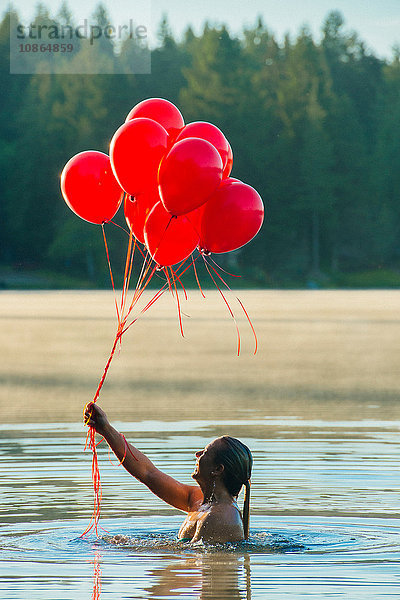 Frau im Wasser hält einen Haufen roter Luftballons