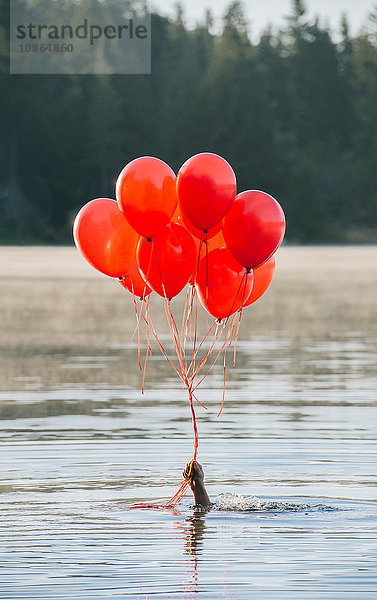 Hand im Wasser mit einem Bündel roter Luftballons