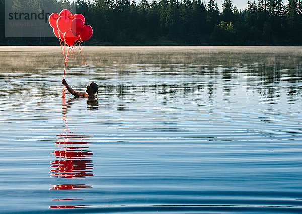 Frau im Wasser hält einen Haufen roter Luftballons