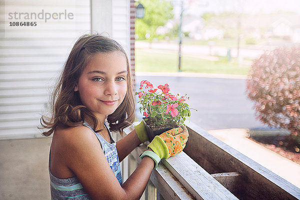 Mädchen pflanzt Blumen in Pflanzkasten und schaut lächelnd in die Kamera