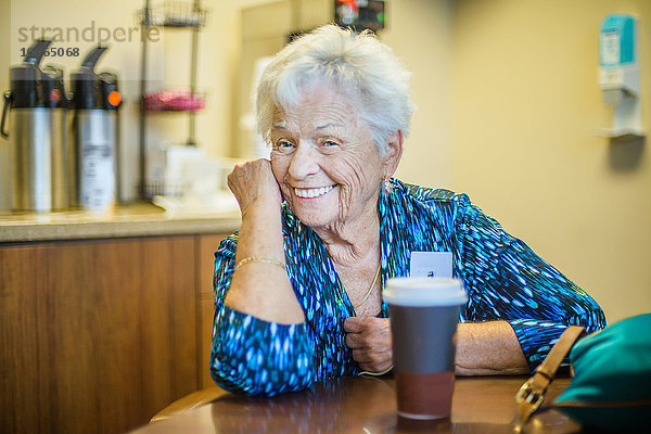 Grauhaarige Frau am Tisch  die lächelnd in die Kamera schaut