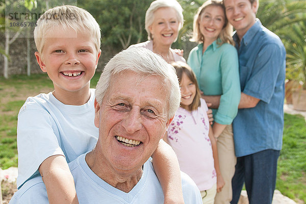 Porträt eines älteren Mannes und seines Enkels vor der Familie  die lächelnd in die Kamera blicken