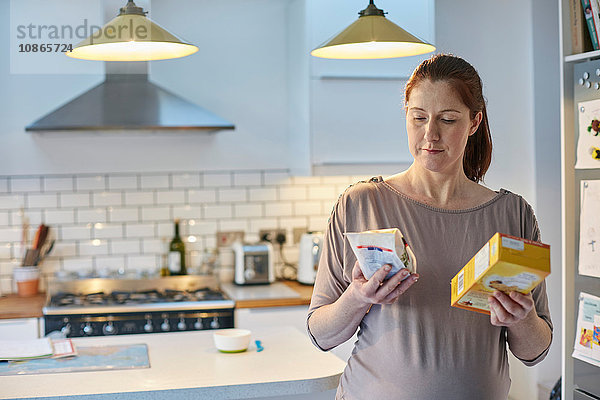 Schwangere Frau in der Küche vergleicht Lebensmittelpakete