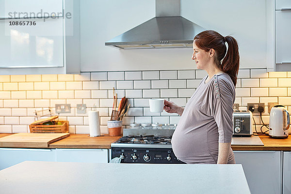 Schwangere Frau in der Küche hält Kaffeetasse
