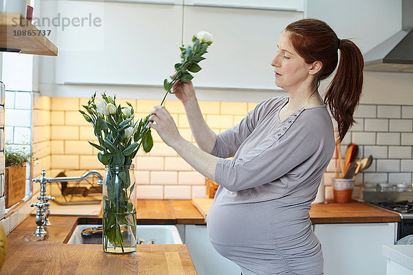 Seitenansicht einer schwangeren Frau in der Küche beim Arrangieren von Blumen in einer Vase