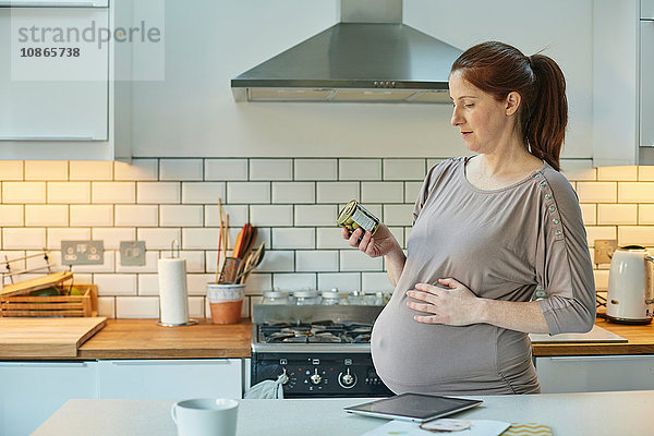 Seitenansicht einer schwangeren Frau in der Küche mit Blick auf Lebensmittelverpackungen