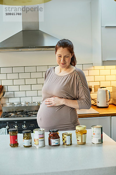 Schwangere Frau in der Küche schaut auf Gläser und Dosen mit Lebensmitteln auf der Küchentheke