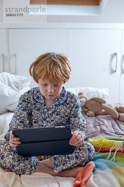 Junge im Schlafanzug mit digitalem Tablett im Bett