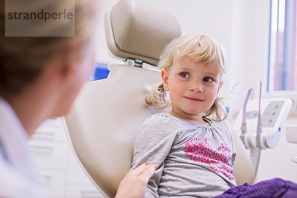 Besorgt aussehendes Mädchen auf Zahnarztstuhl im Gespräch mit Zahnarzt