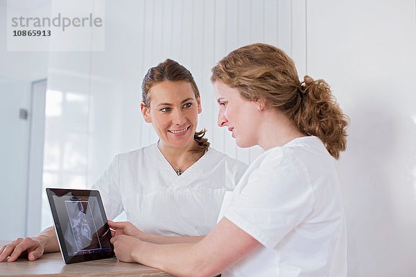 Zahnärzte schauen lächelnd auf ein digitales Tablett mit Röntgenbild auf dem Bildschirm