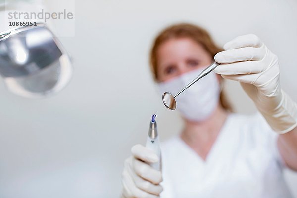 Niedrigwinkelansicht eines Zahnarztes  der eine Maske und Schutzhandschuhe trägt und eine zahnärztliche Ausrüstung und einen Zahnarztspiegel hält