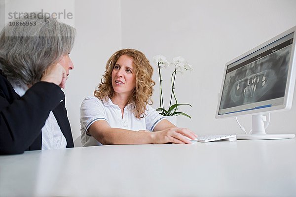 Oberflächenansicht einer reifen Frau und einer älteren Frau  die über ein Röntgenbild auf einem Computerbildschirm diskutieren