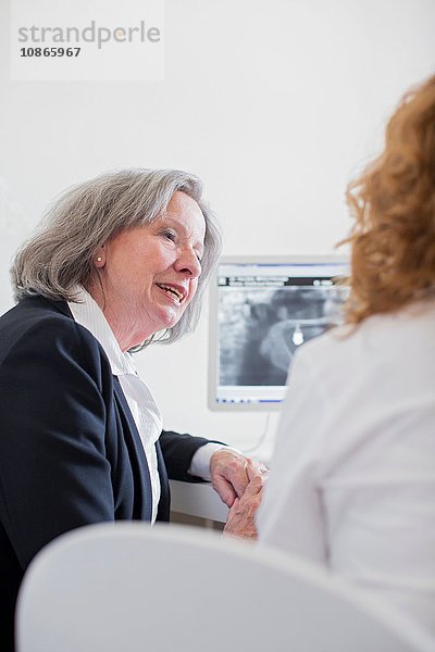 Ältere Frau bespricht Röntgenbild am Computerbildschirm
