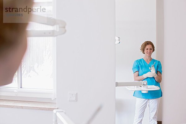 Zahnarzthelferin in Zahnklinik trägt Schutzhandschuhe und bereitet Spritze lächelnd vor