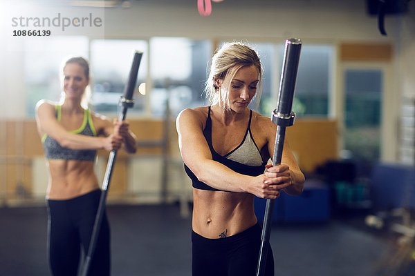 Zwei weibliche Crossfitterinnen trainieren mit Metallstangen in der Turnhalle