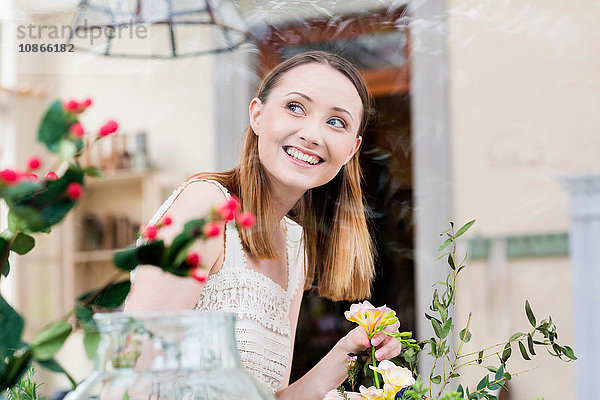 Blick durch das Glas einer Frau  die Blumen arrangiert und lächelnd wegschaut
