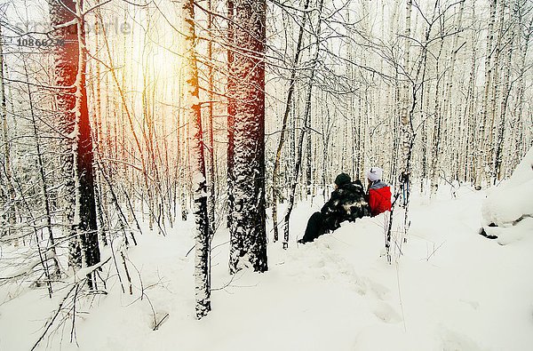 Ehepaar sitzt im verschneiten Wald und betrachtet den Sonnenuntergang  Russland