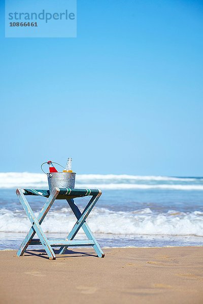 Glasflaschen mit Saft im Eiskübel auf Liegestuhl am Strand