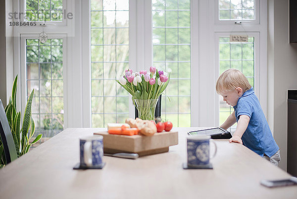 Junge steht am Tisch und schaut auf digitales Tablett