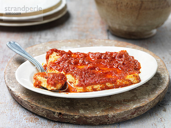Gebackener Feta-Käse mit sonnengetrockneter Tomatensauce  in Schüssel mit Löffel