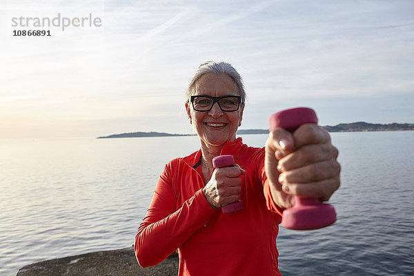 Reife Frau am Wasser  mit Handgewichten trainierend  lächelnd