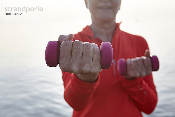 Reife Frau am Wasser  mit Handgewichten trainierend  Mittelteil