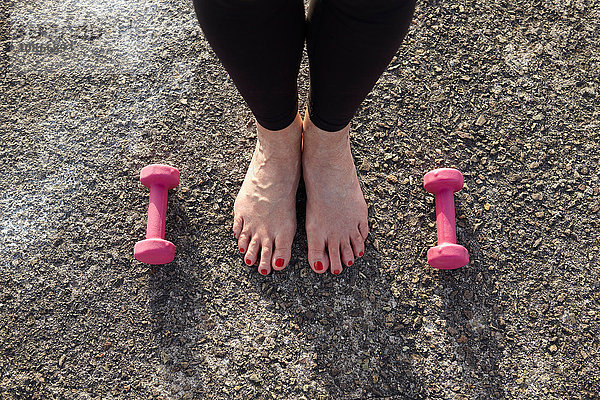 Reife Frau steht barfuß  Handgewichte auf dem Boden neben ihr  erhöhte Ansicht  Fokus auf Füße
