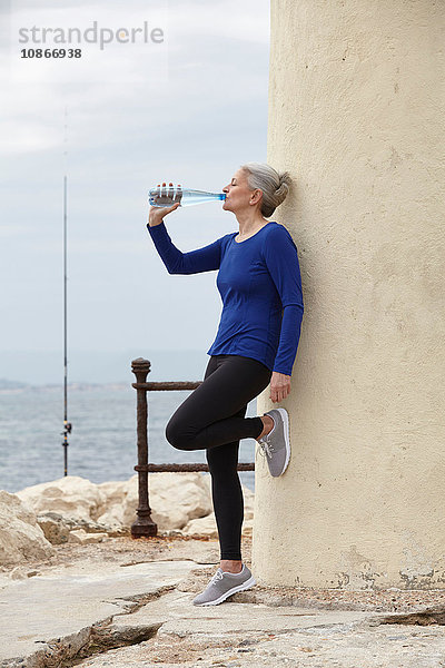 Reife Frau im Freien  an die Wand gelehnt  aus Wasserflasche trinken
