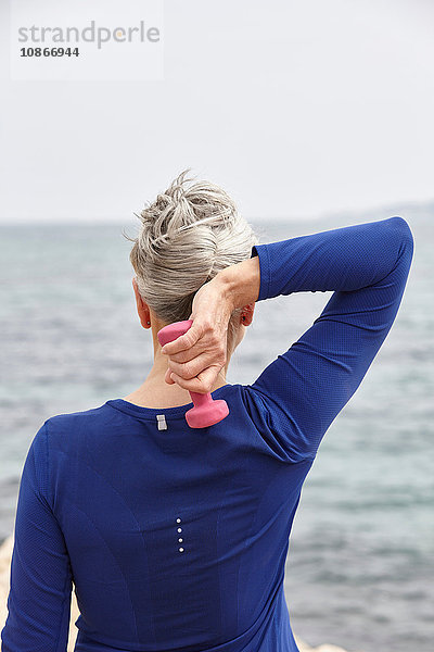 Reife Frau am Meer  mit Handgewichten trainierend  Rückansicht